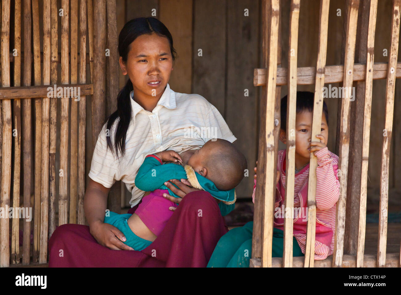 A woman of the AKHA tribe nurses a child in her bamboo house - village near KENGTUNG or KYAINGTONG - MYANMAR Stock Photo