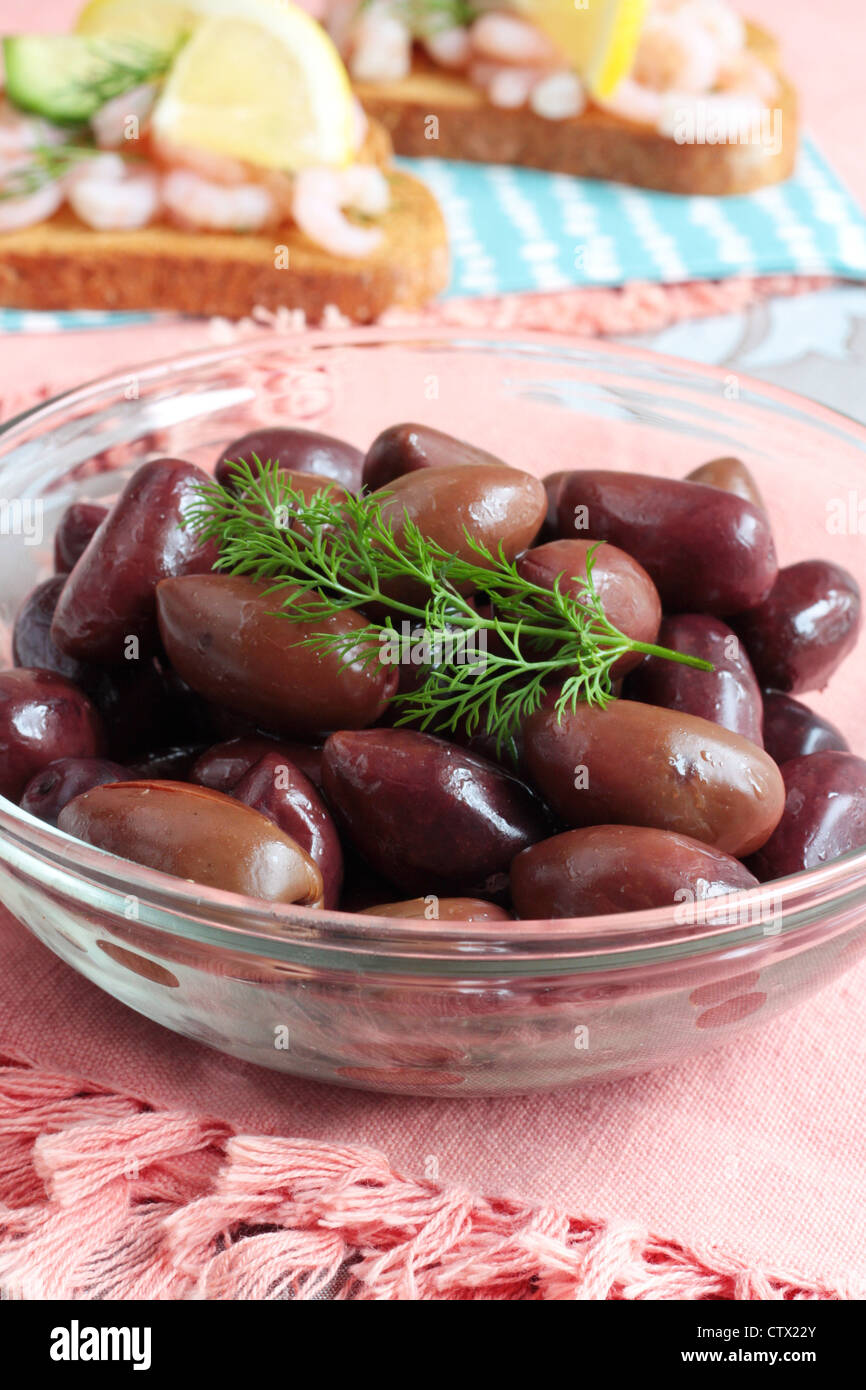 A dish of black Kalamata olives with prawn appetizers in the background Stock Photo