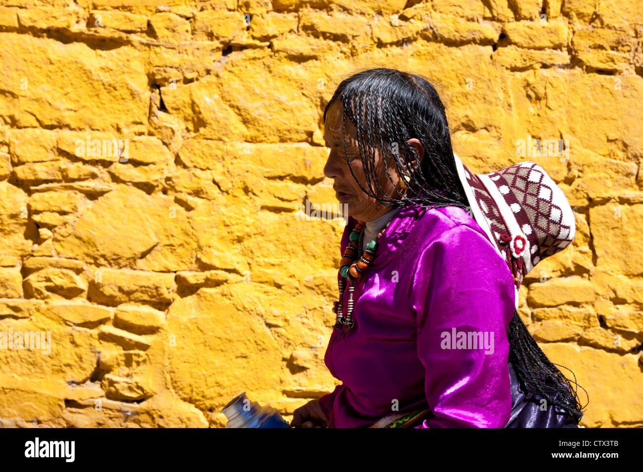 A Tibetan woman wearing traditional clothes is passing a yellow wall, Tibet, Stock Photo