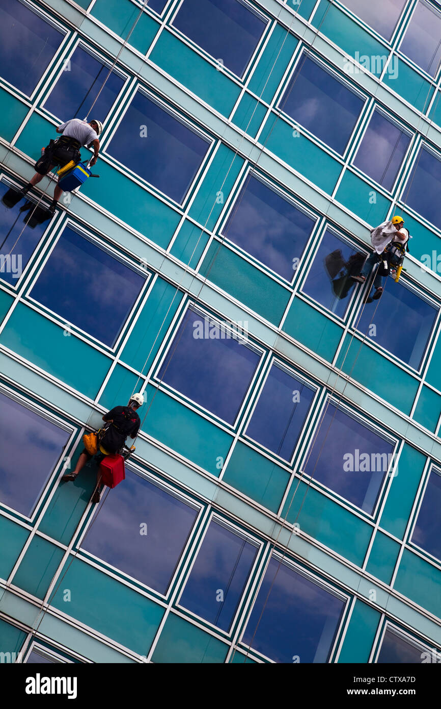 Three window cleaners suspended by ropes on an office building in