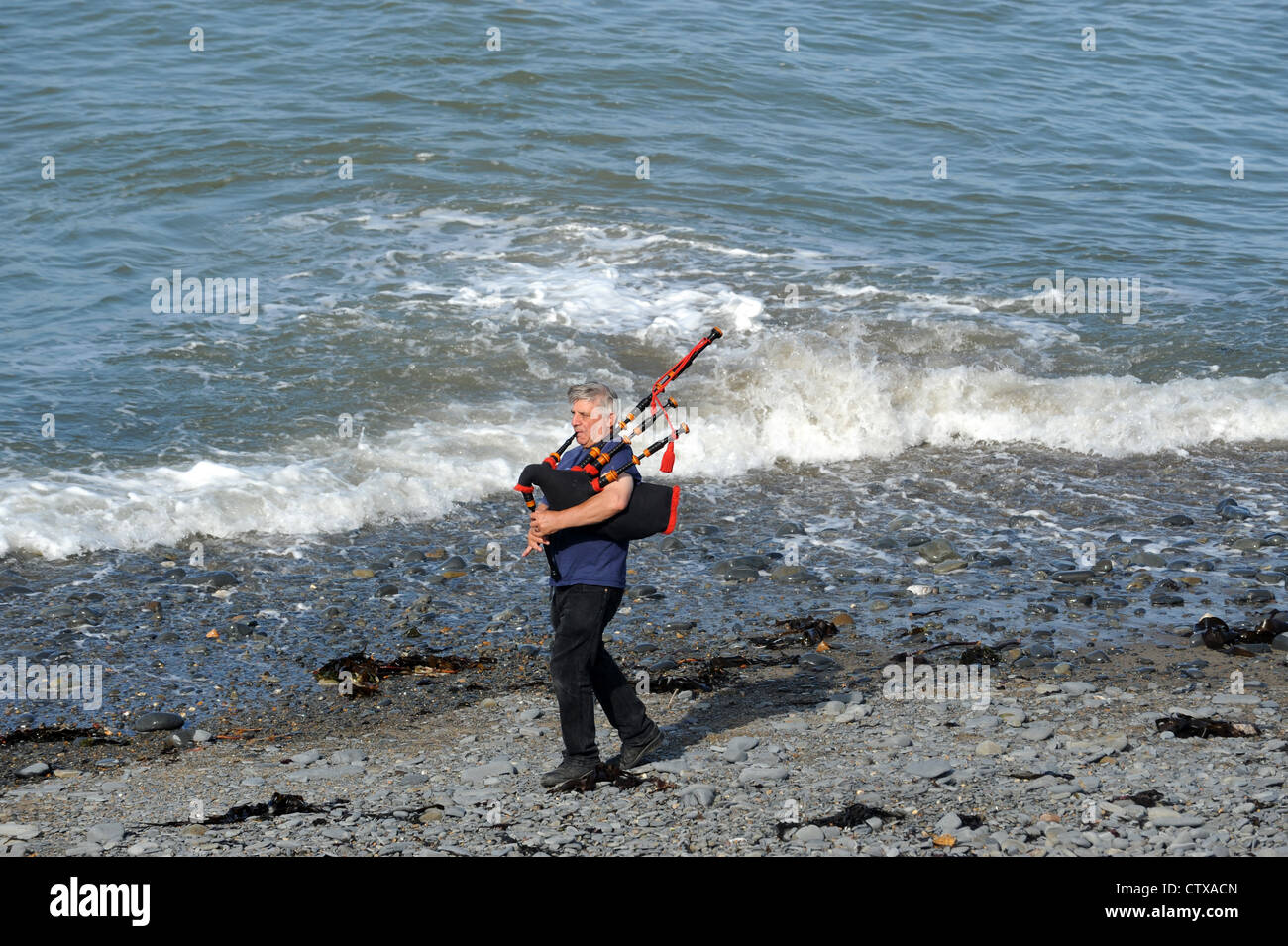 Man playing bagpipes on the beach at Clarach Bay near Aberystwyth in Wales Stock Photo