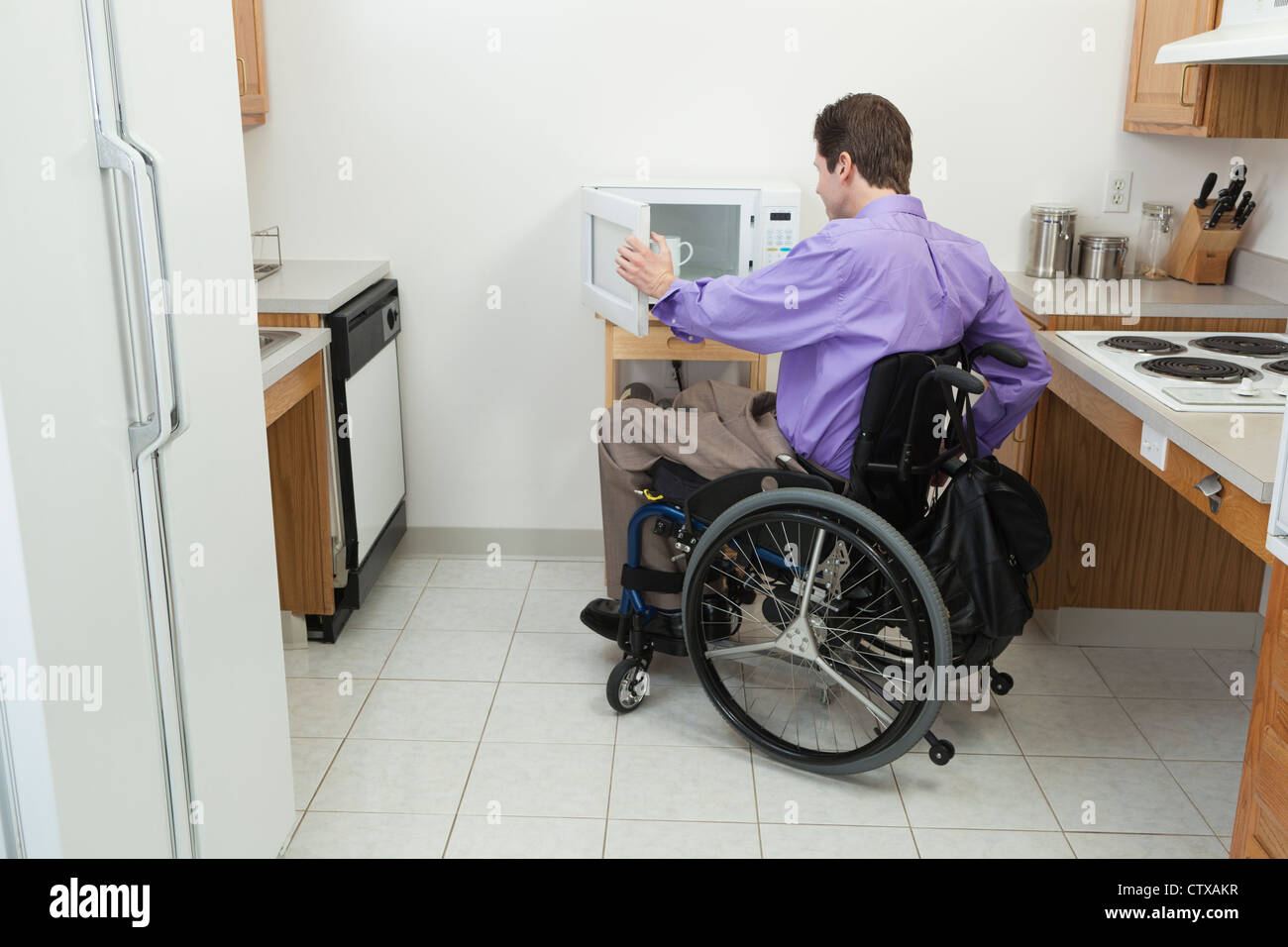Man in wheelchair with spinal cord injury opening accessible microwave ...