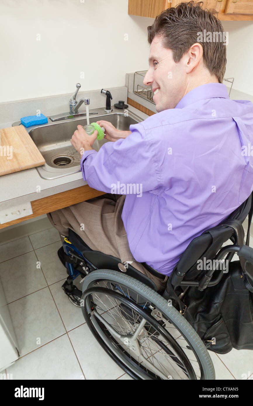 Man in wheelchair with spinal cord injury washing glass in an accessible kitchen sink Stock Photo