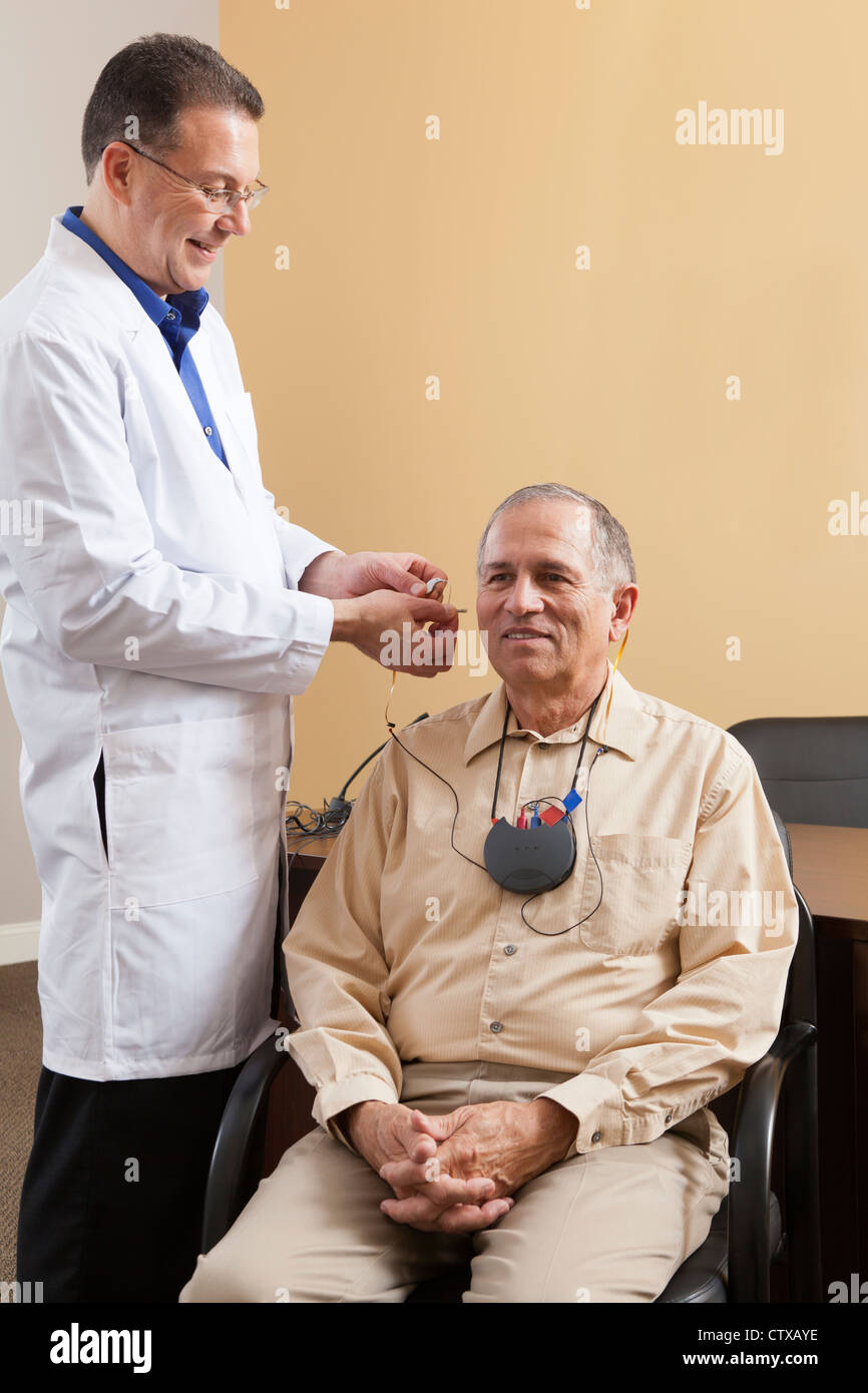 Audiologist Inserting Behind The Ear Hearing Aid Into A Patients Ear During Programming Stock