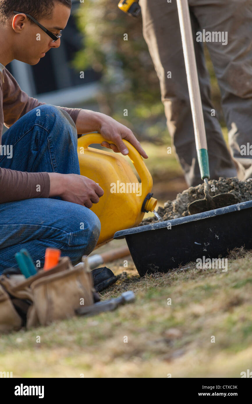 Hispanic carpenter adding water to concrete mix for new deck footing