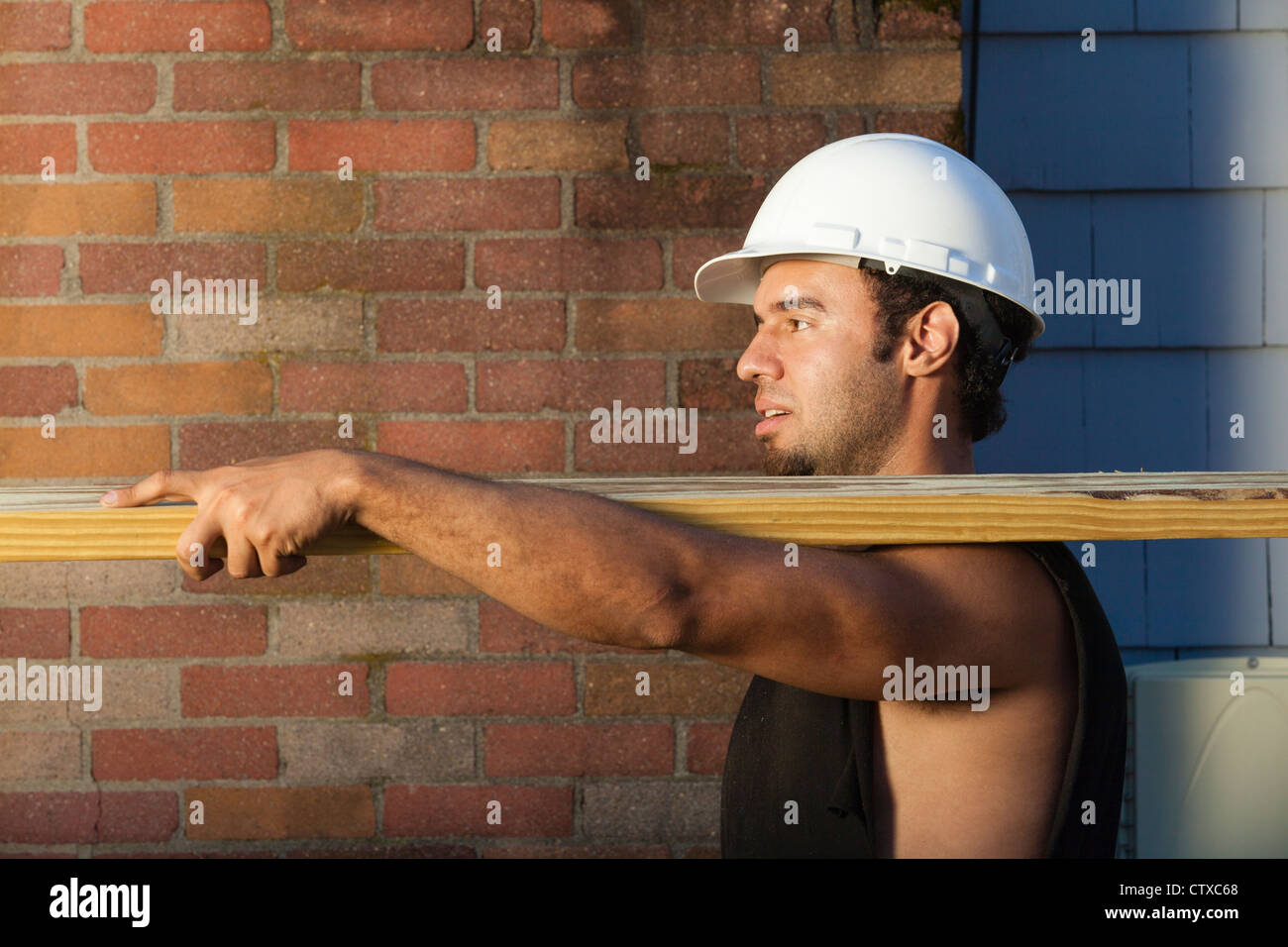 Hispanic carpenter carrying pressure treated lumber at house site Stock Photo