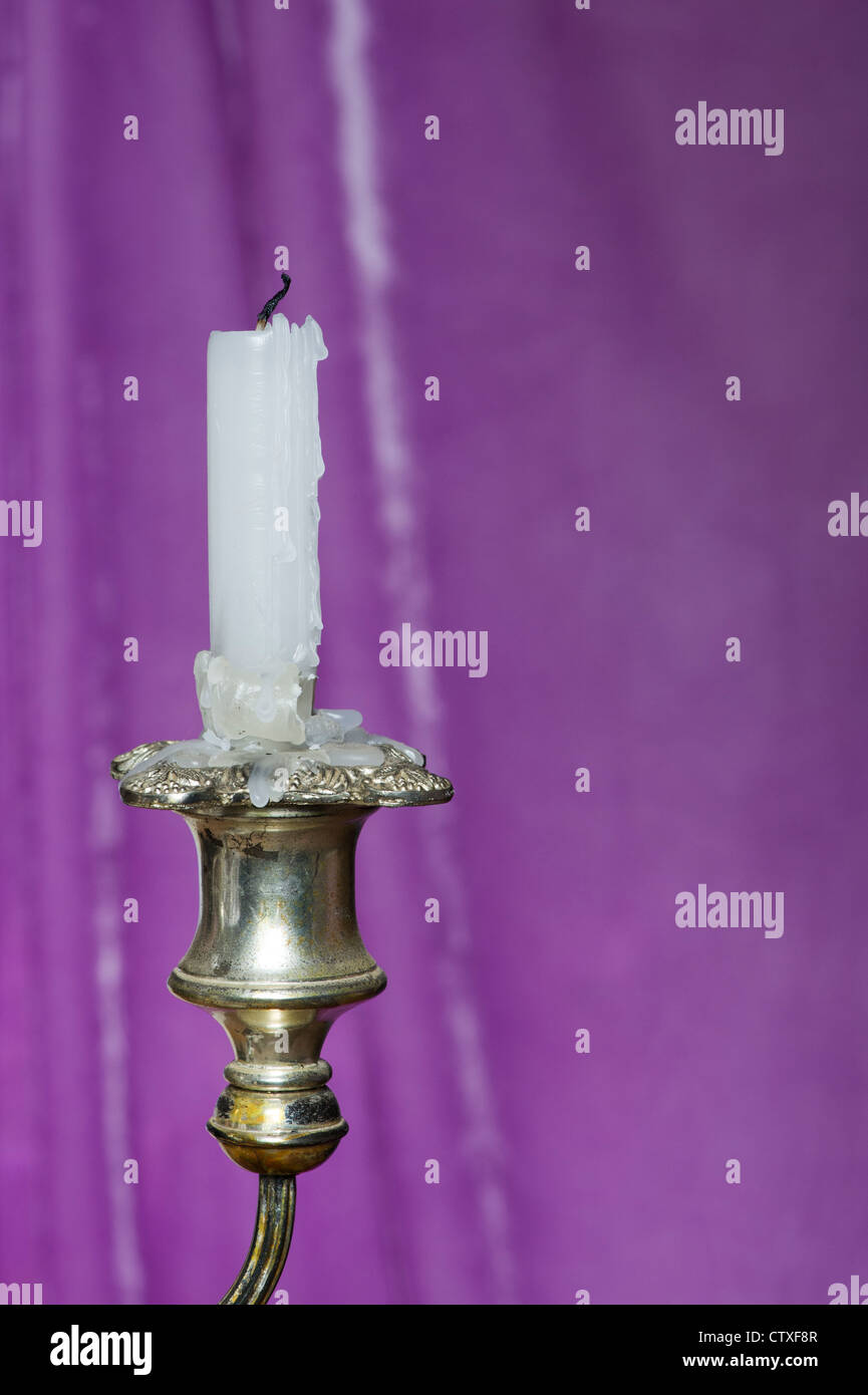 Candle in an old candle stick in front of a purple drape Stock Photo