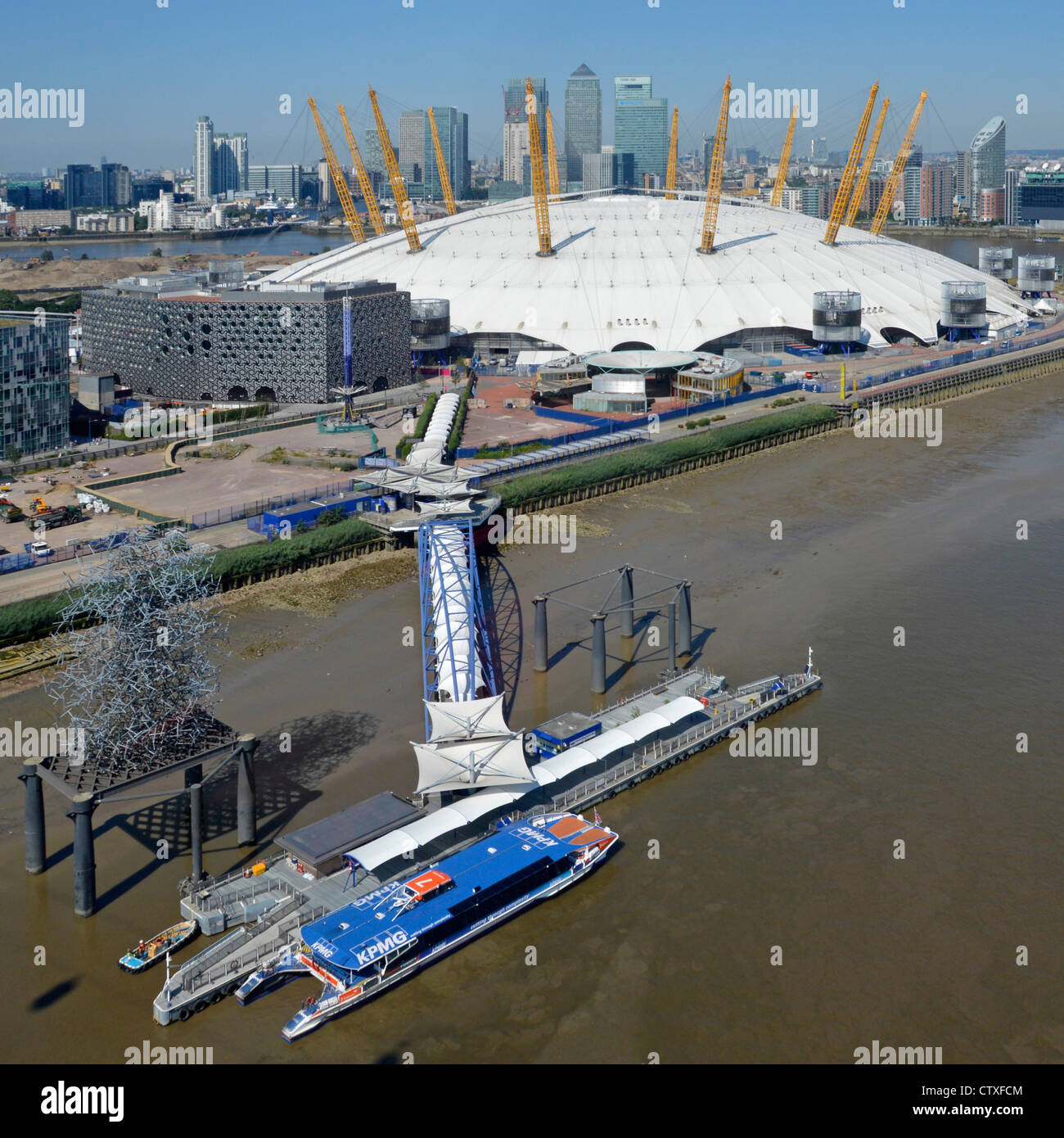 Aerial view of North Greenwich Peninsula & Pier Thames Clipper river bus beside O2 arena millenium dome 2000 & Canary Wharf skyline beyond London UK Stock Photo