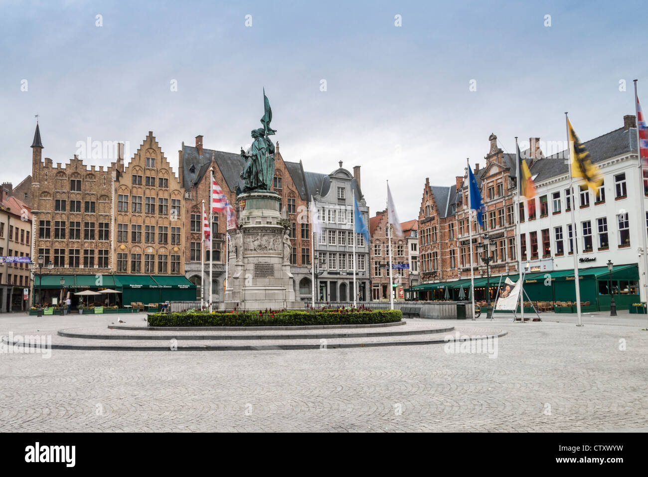 Flags flying around a statue of Jan Breydel and Pieter de Coninck early morning in Brugge Market Square Stock Photo