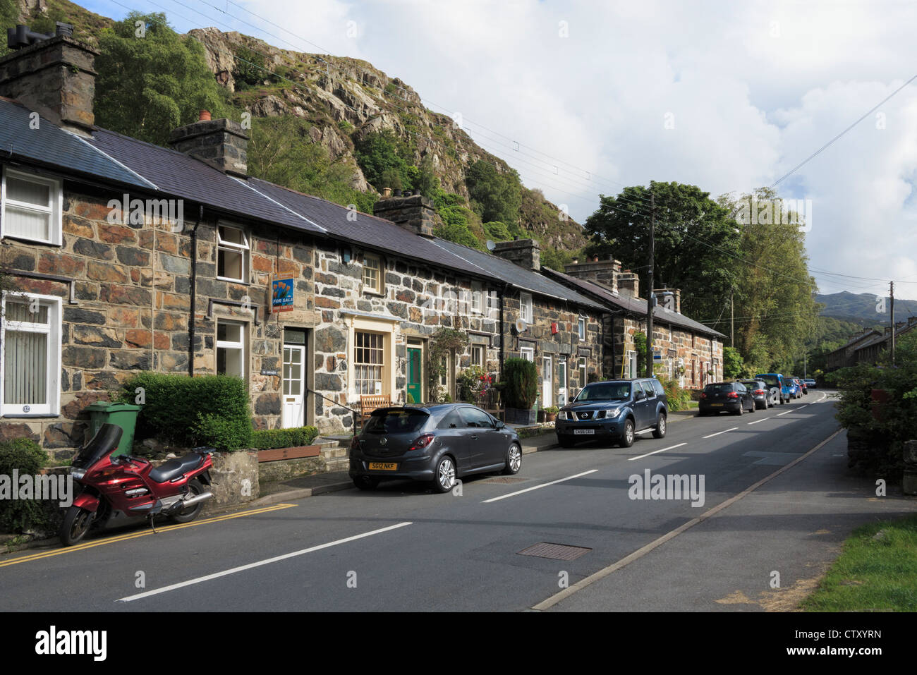 Row of terraced houses with cars parked outside on narrow main road through Beddgelert in Snowdonia National Park North Wales UK Stock Photo