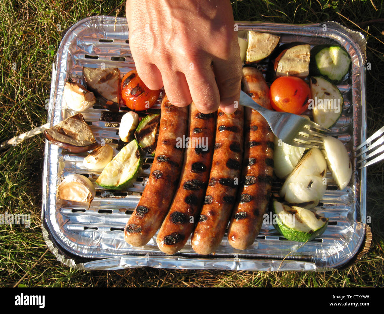 Hands on a disposable barbecue with sausages and vegetables Stock Photo