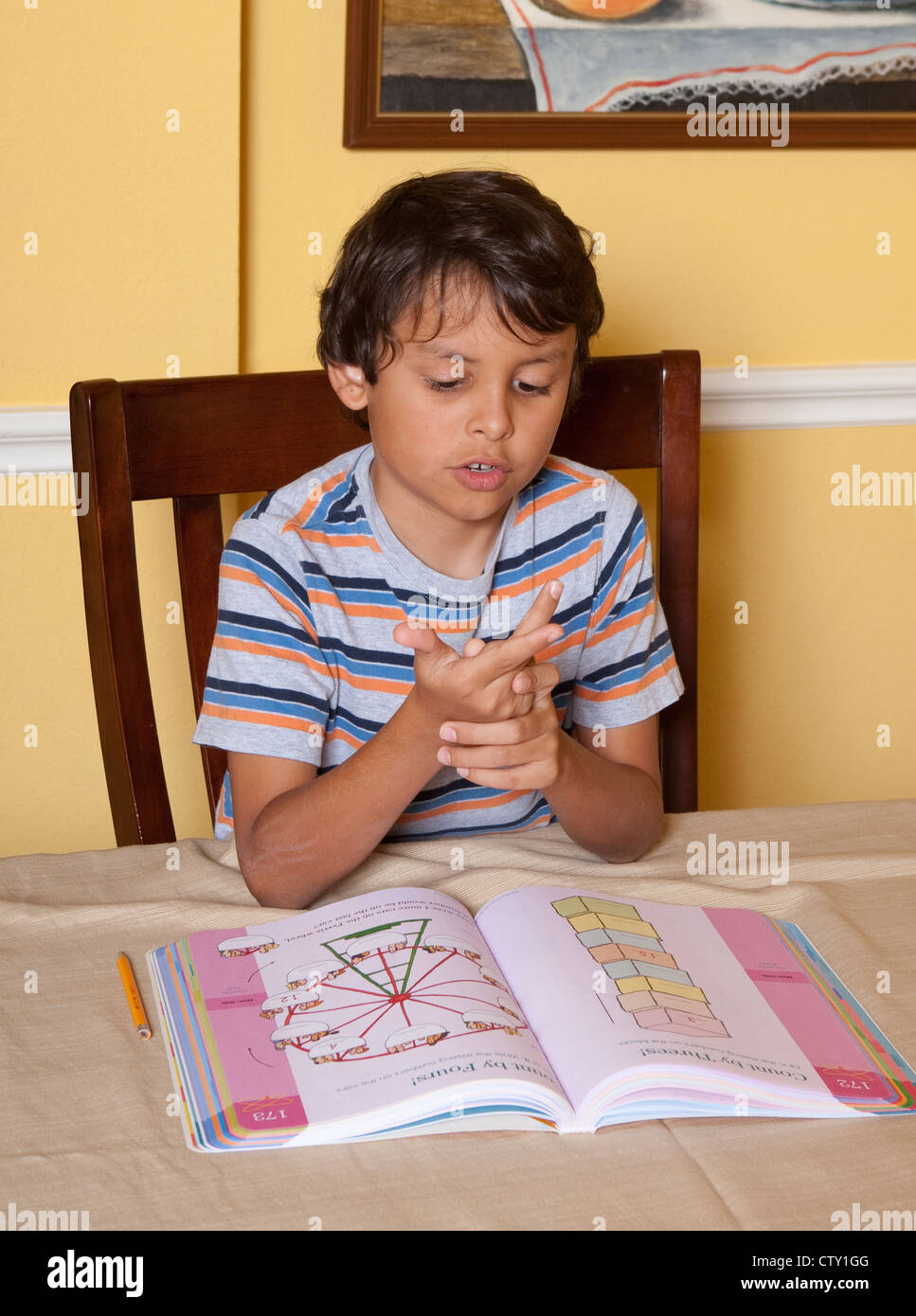 8 year old Mexican-American elementary school age boy uses fingers to help count while doing math school work while at home Stock Photo