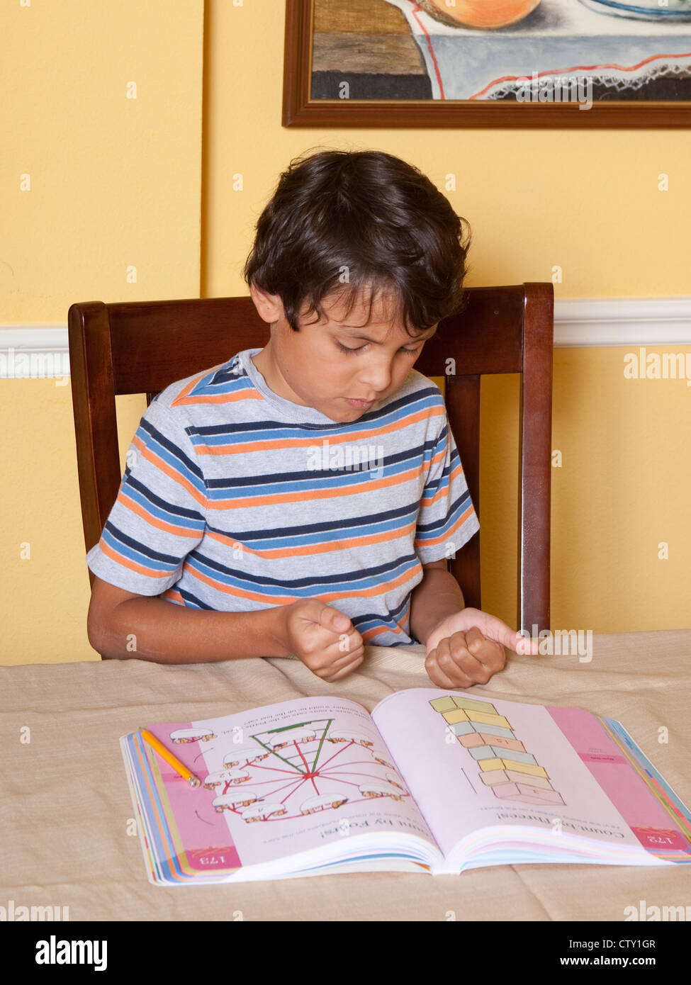 8 year old Mexican-American elementary school age boy uses fingers to help count while doing math school work while at home Stock Photo