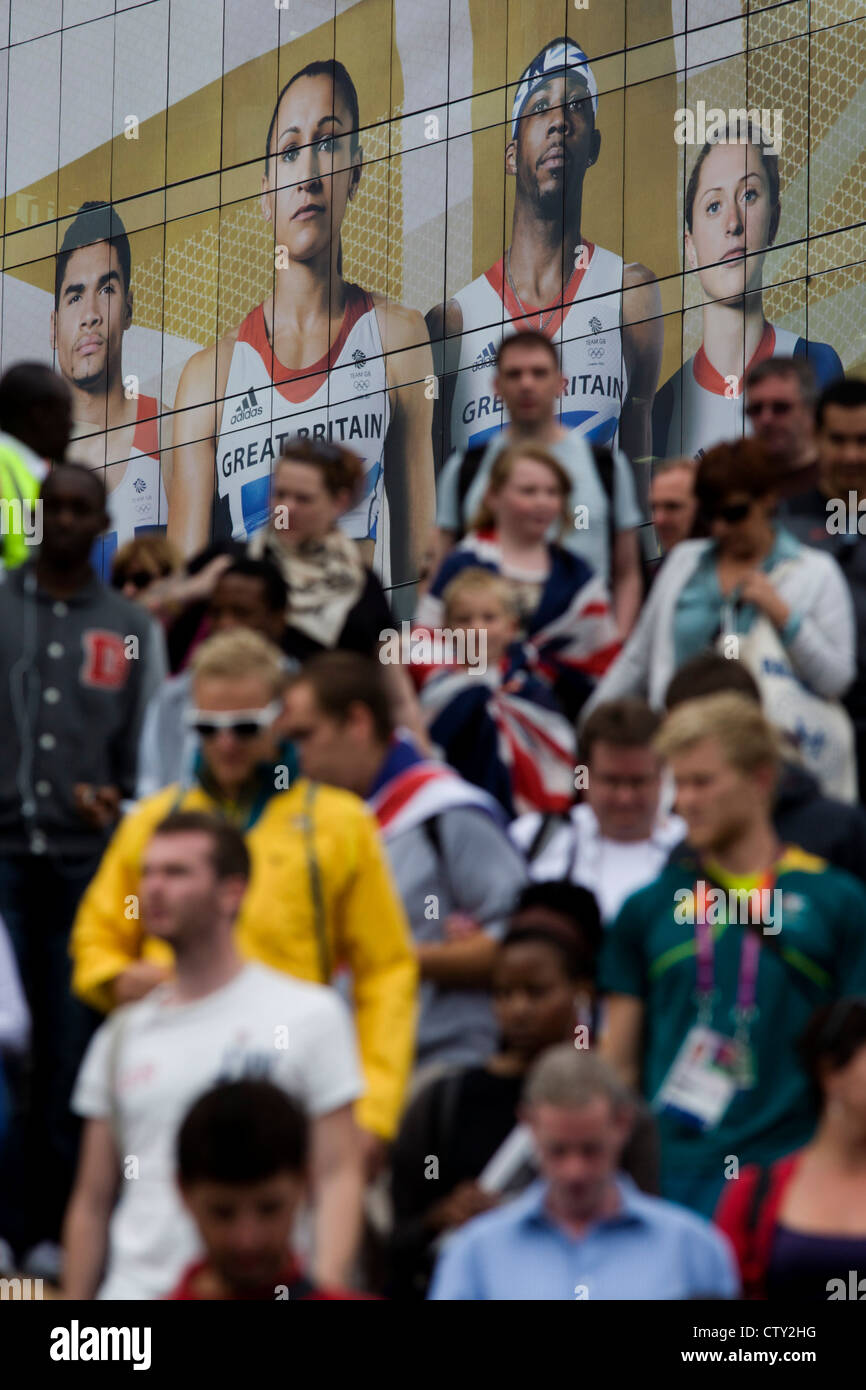 With giant presence of Team GB role-model athlete heroes behind them, spectator crowds descend steps at the Westfield City shopping complex, Stratford that leads to the Olympic Park during the London 2012 Olympics, the 30th Olympiad. The ad is for sports footwear brand Adidas and their 'Take the Stage' campaign including diver Tom Daley, gymnast Louis Smith, triple jumper Phillips Idowu and the darling of British athletics, heptathlete gold medalist Jessica Ennis. Stock Photo