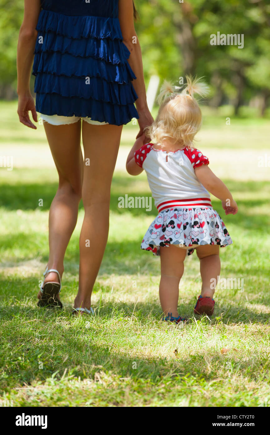 Mother holding hand of her female toddler while walking in a park Stock ...