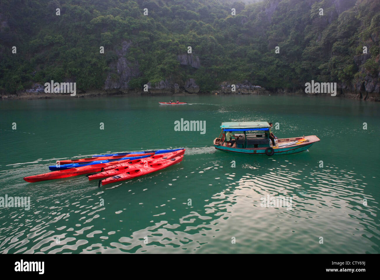 Small boat towing colorful kayaks, Halong Bay, Vietnam Stock Photo