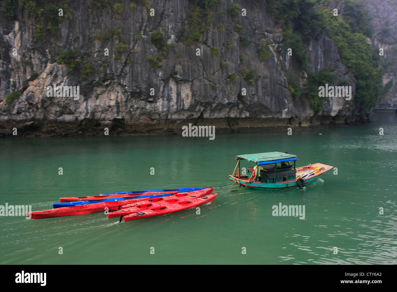 Small boat towing colorful kayaks, Halong Bay, Vietnam Stock Photo