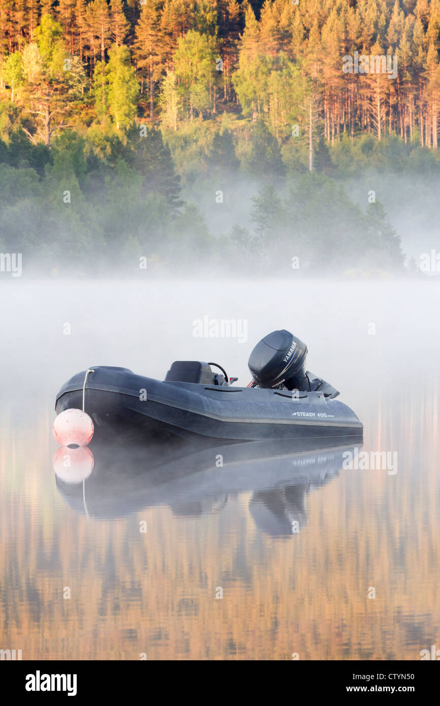 A lone dinghy floats motionless in the mist at dawn on Loch Morlich, Glenmore, The Cairngorms, Scotland. Stock Photo