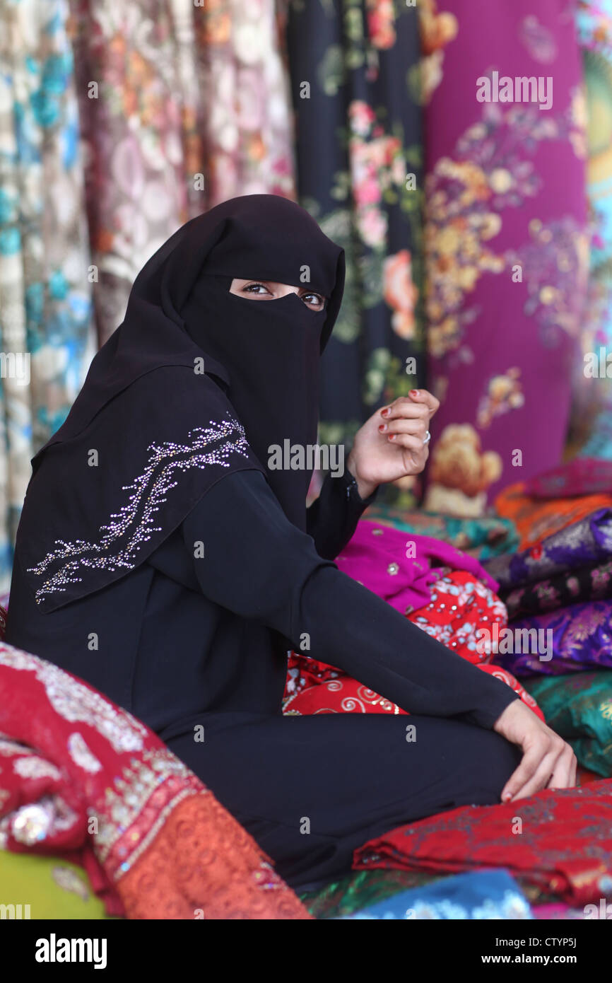 Muslim woman, with hidden face behind veil, selling clothes in her own business shop Stock Photo