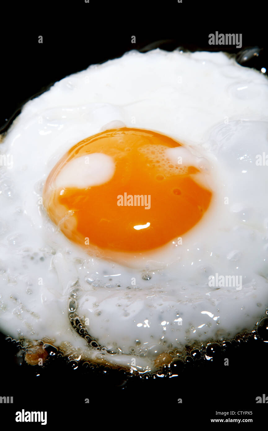cooking frying egg with yolk on black pan Stock Photo