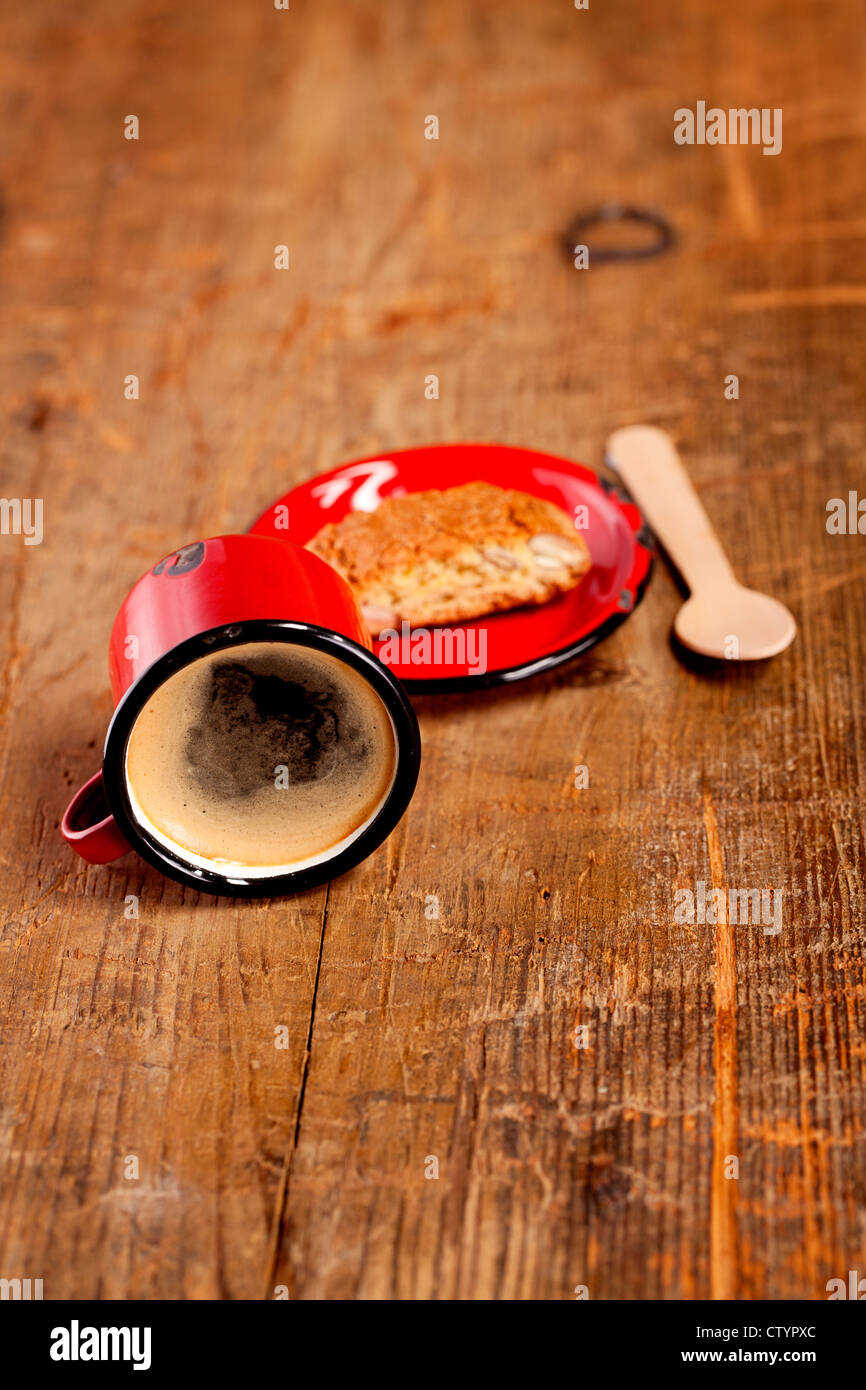 extremely overturned espresso coffee in red enamel mug with saucer, wooden spoon and Cantuccini Biscotti Stock Photo