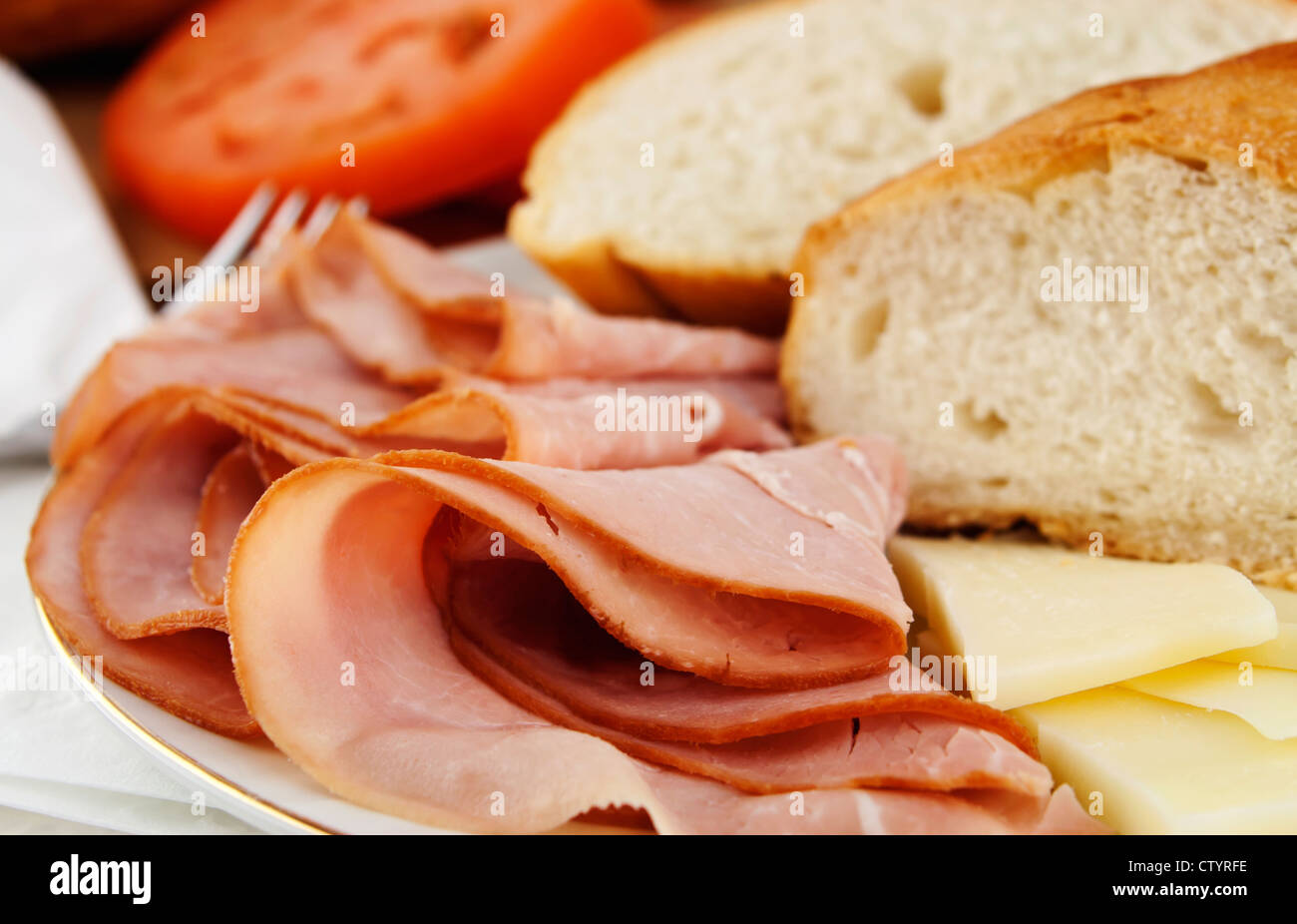 Delicious lunch time spread with ham, bread, cheese and tomatoes with silver fork. Stock Photo