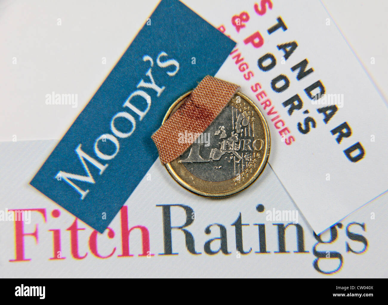 An 'injured' or 'damaged' or 'wounded' one Euro coin with the logos for the three credit rating agencies behind. Stock Photo