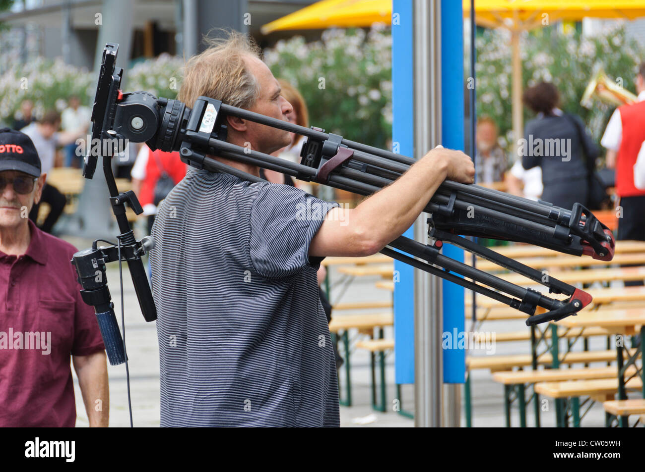 Caucasian male camera crew member carries a professional TV camera tripod on his shoulder Stock Photo