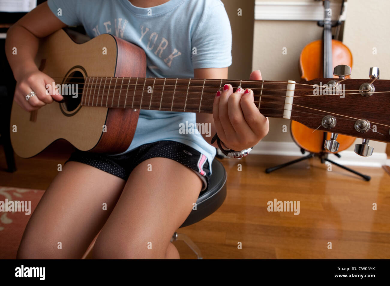 Japanese-American 10 year old girl practices playing guitar, uses sheet music while at home. Stock Photo