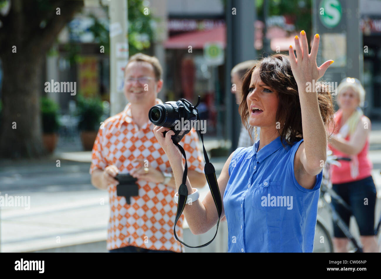 Young angry woman brown hair in blue shirt carrying a NIKON D5000 DSLR flourishing with hand up and yellow varnished fingernails Stock Photo