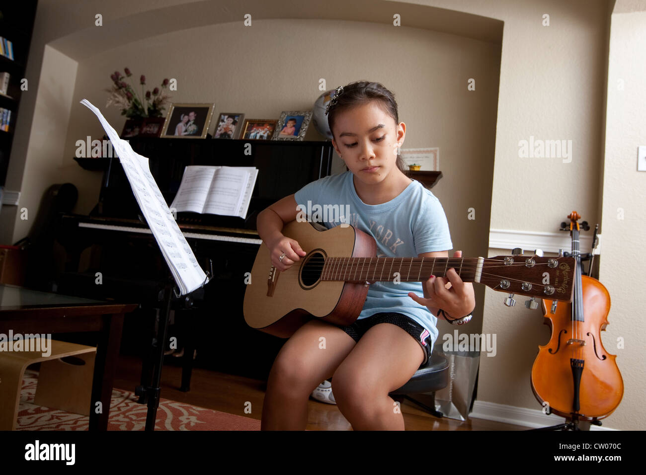 Japanese-American 10 year old girl practices playing guitar, uses sheet  music while at home Stock Photo - Alamy