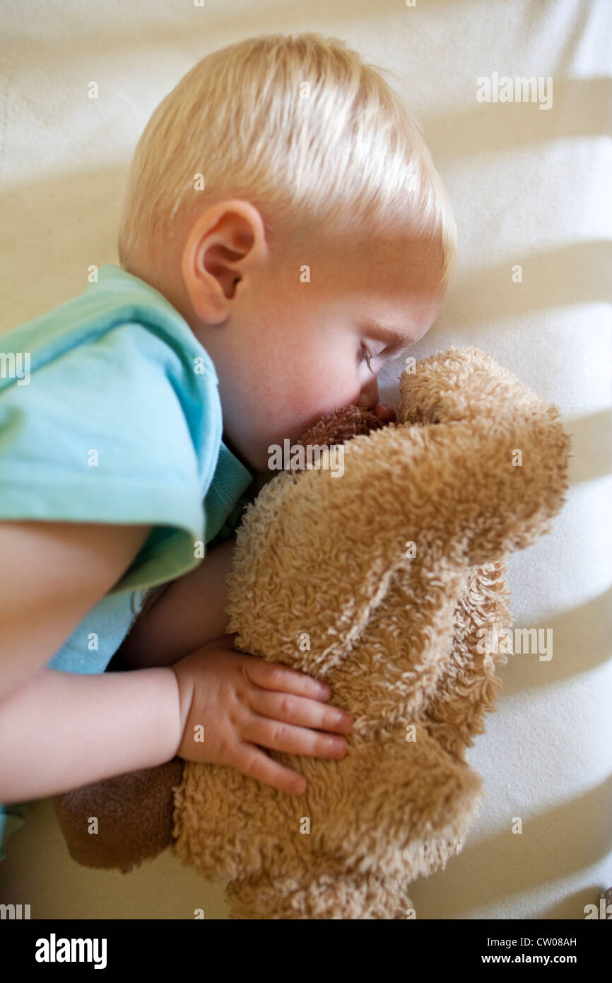 20 month old baby boy asleep whilst holding cuddly toy in cot Stock Photo