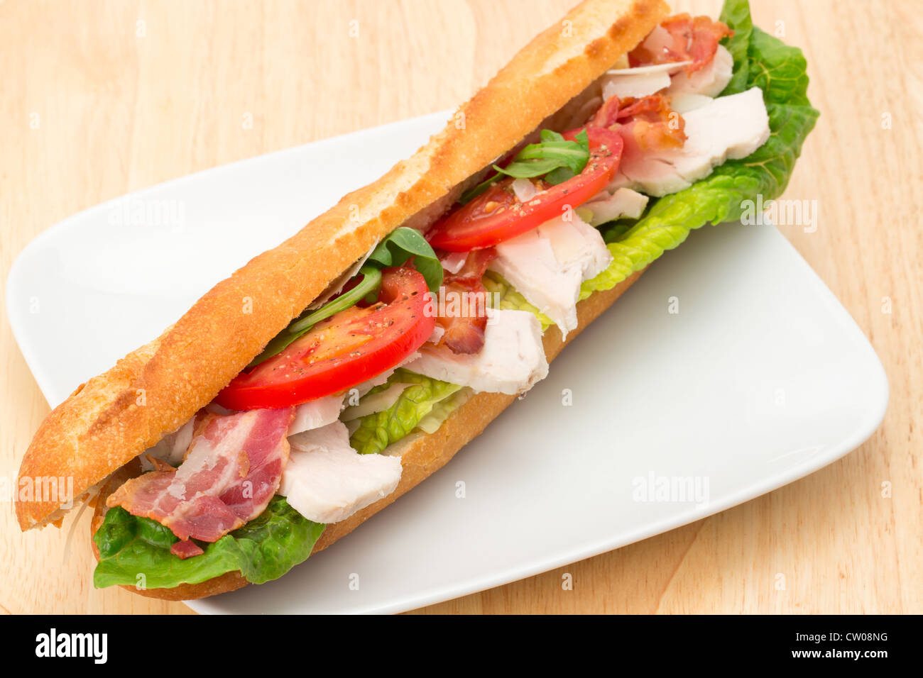 Chicken, bacon and salad filled baguette served on a white plate - studio shot Stock Photo