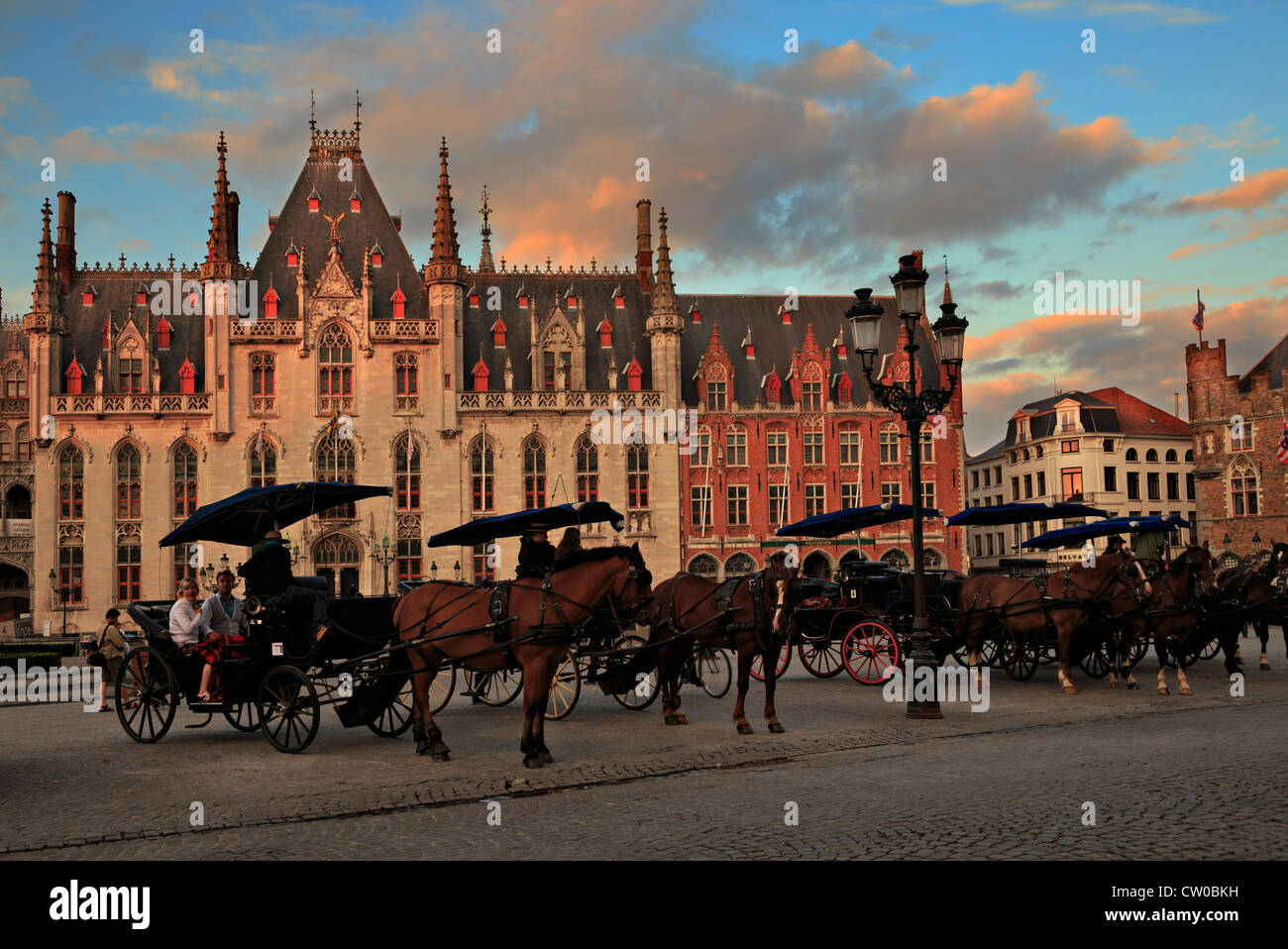 The Government Palace is lit by the evening light as horse drawn carriages wait for tourists in Bruges, Belgium Stock Photo