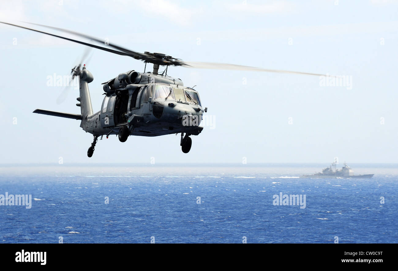 An MH-60S Seahawk helicopter assigned to the Golden Falcons of Helicopter Sea Combat Squadron (HSC) 12 flies past the Ticonderoga-class guided-missile cruiser USS Cape St. George (CG 71) during an air power demonstration over the Nimitz-class aircraft carrier USS Abraham Lincoln (CVN 72). Lincoln is en route to the United States to complete an eight-month change-of-homeport deployment during which it operated in the U.S. 5th, 6th and 7th Fleet areas of responsibility. Stock Photo