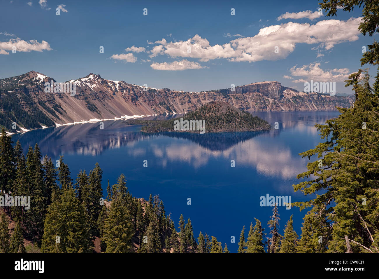 Afternoon clouds and Wizard Island reflect in the calm water of Oregon’s Crater Lake National Park. Stock Photo