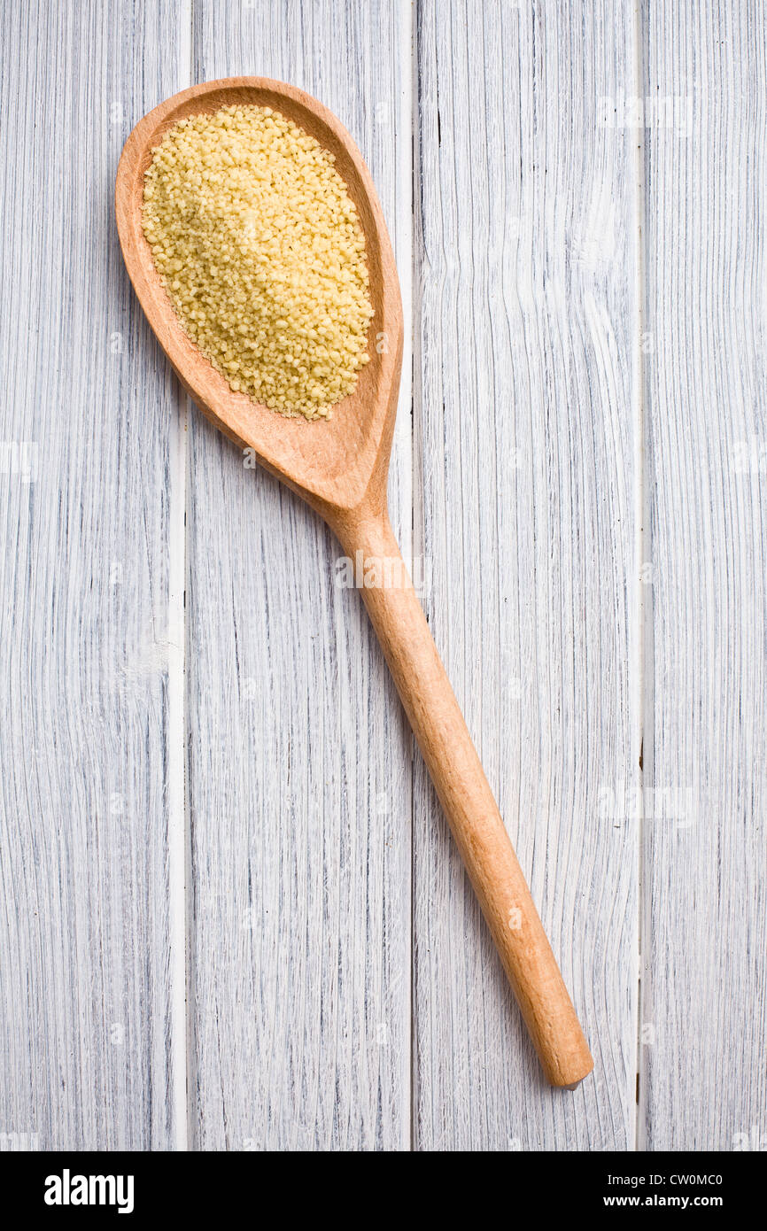couscous in wooden spoon on kitchen table Stock Photo