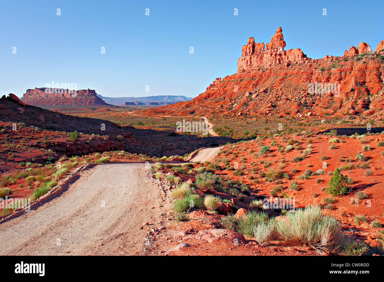 Dirt road in desert heading into the distance in undulating terrain with rock formations in background and shrubs in foreground Stock Photo