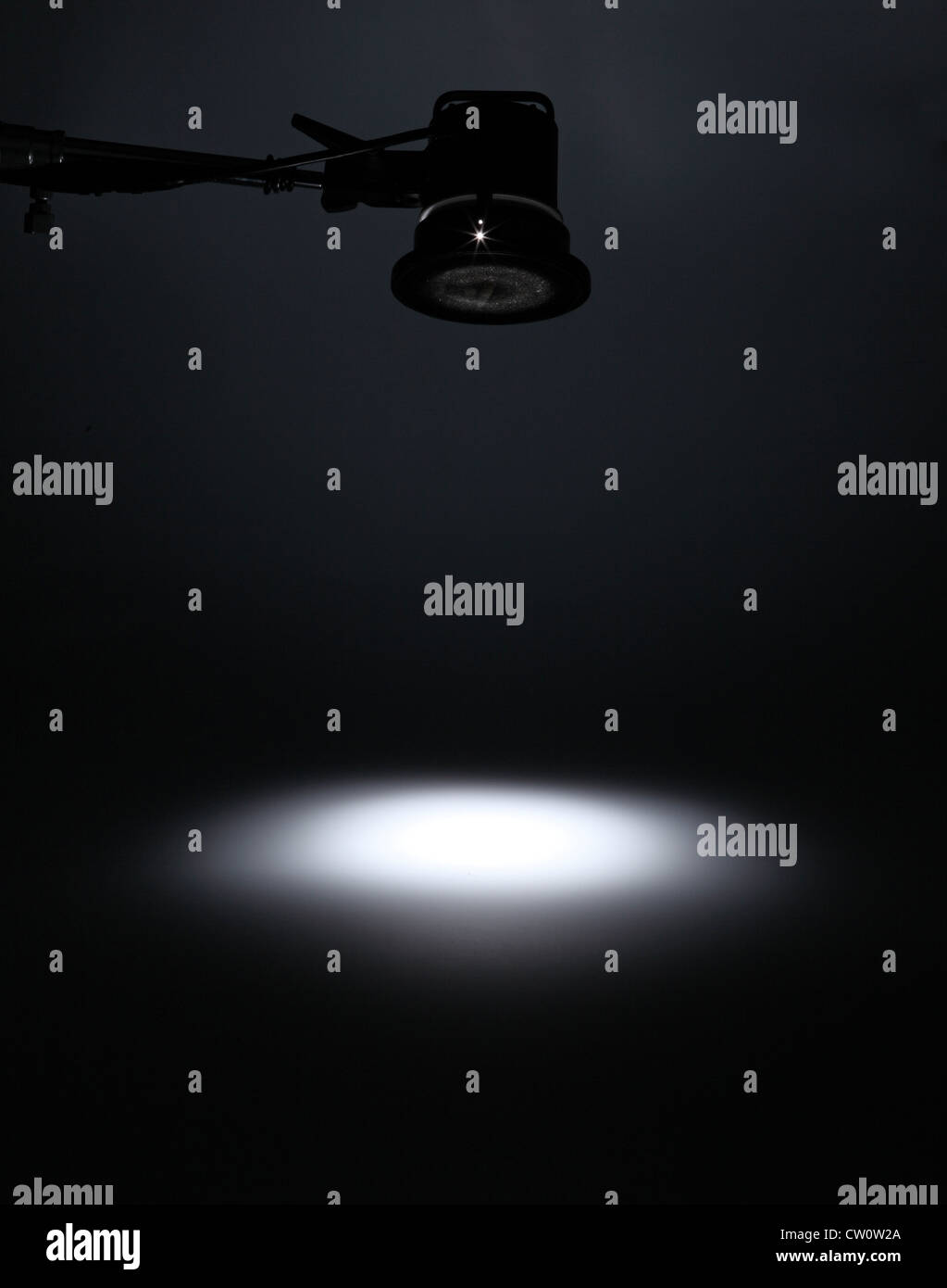 A photographic light from above creating a white spotlight on an empty dark background. Stock Photo