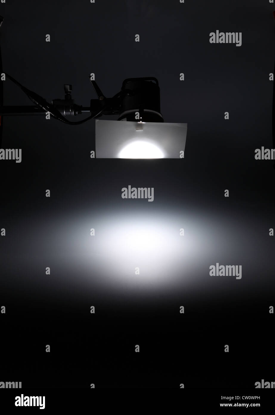A photographic light from above creating a white spotlight on an empty dark background. Stock Photo