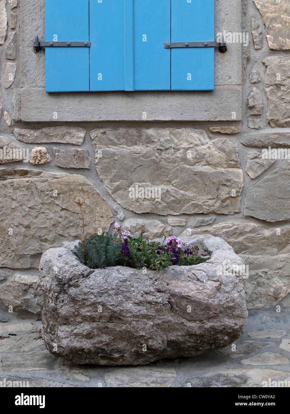Stone planter with flowers in front of stone house with blue window ...