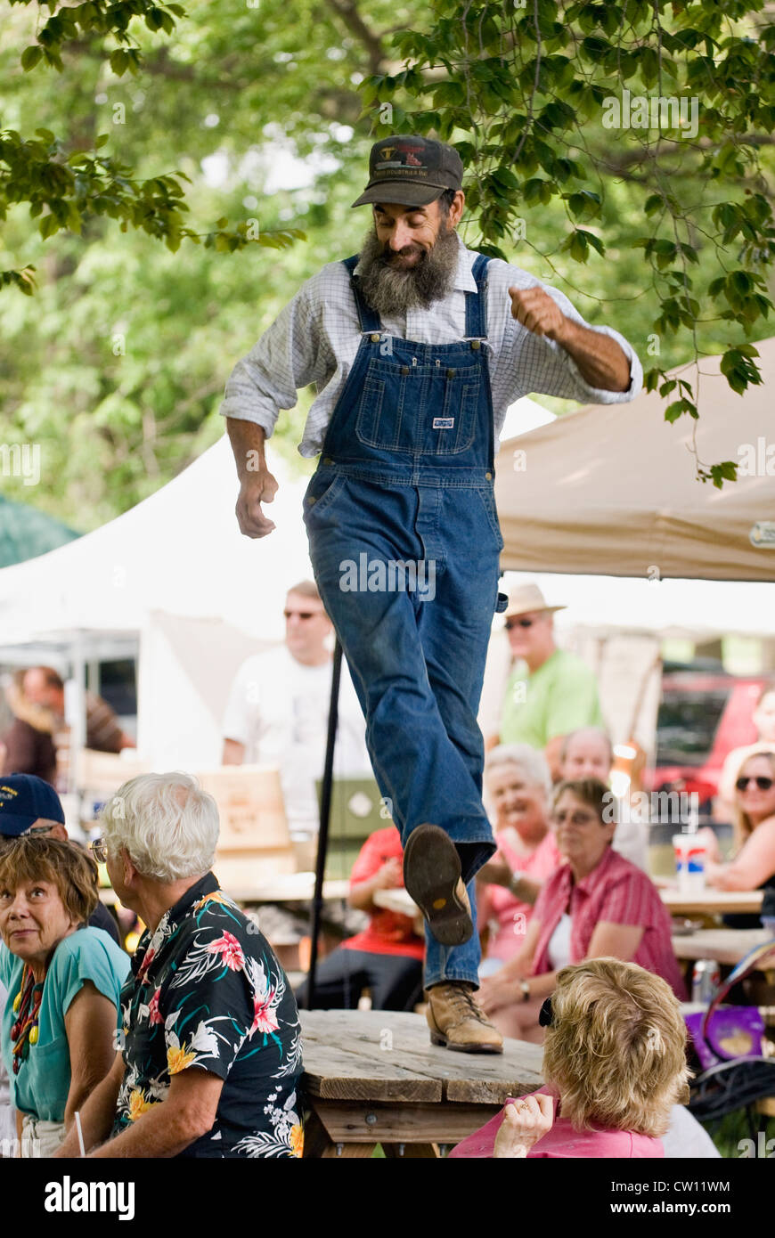 Man in Bib Overalls Dancing a Jig on a Picnic Table Amid Crowd at the Kentucky Music Festival at