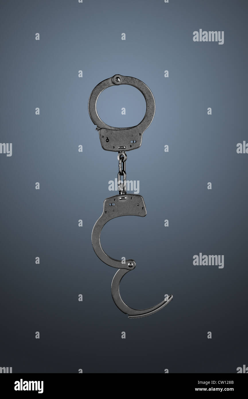 Handcuffs hanging against a Grey gradient background. Stock Photo