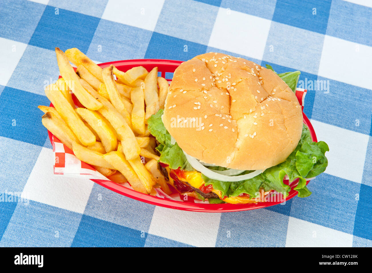 A top down view of a hamburger with fries in a red basket on a picnic tablecloth. Stock Photo