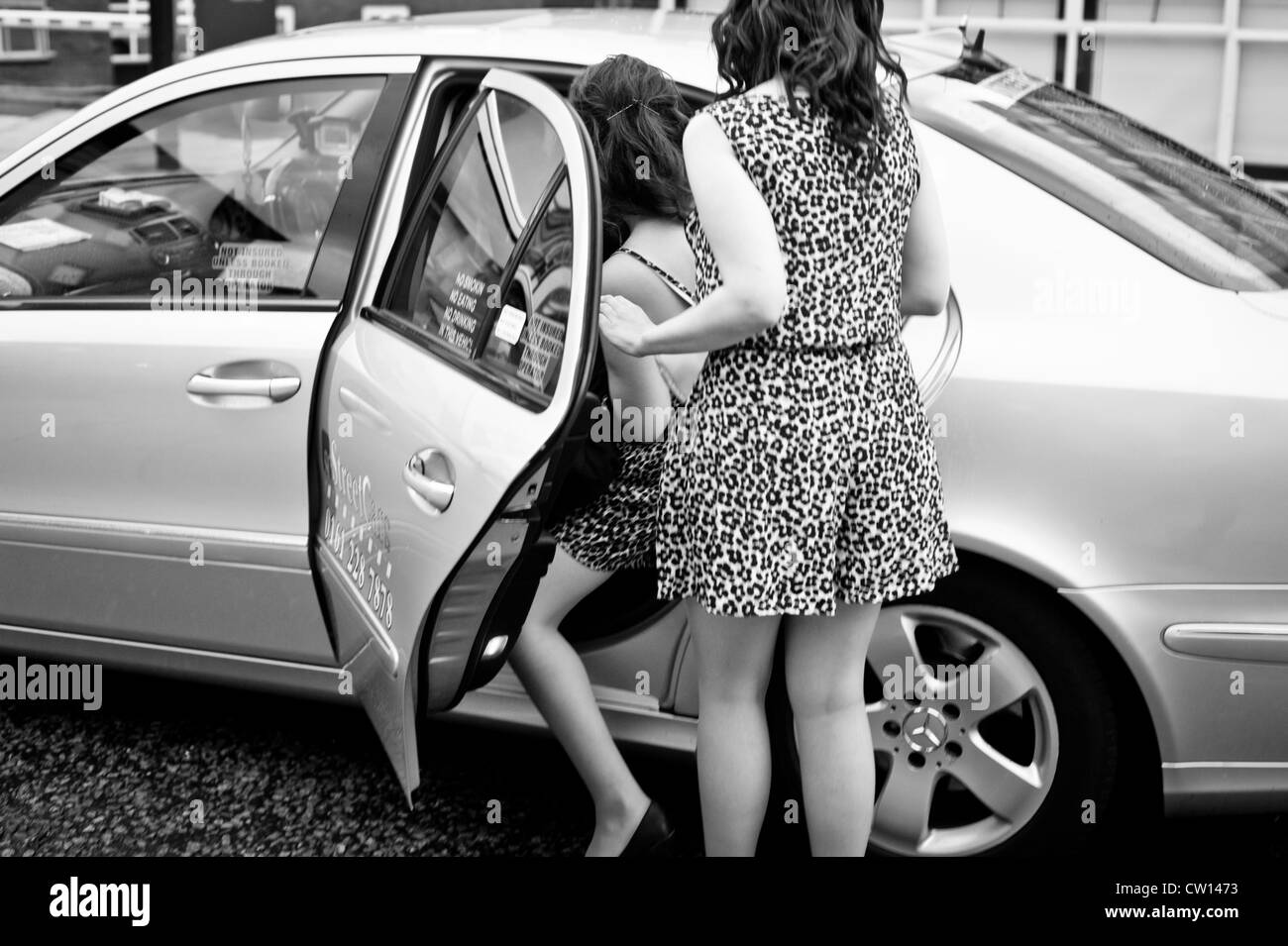Manchester, UK - 4 August 2012: two leopardskin dressed girls get into a cab getting ready for a night out. Stock Photo