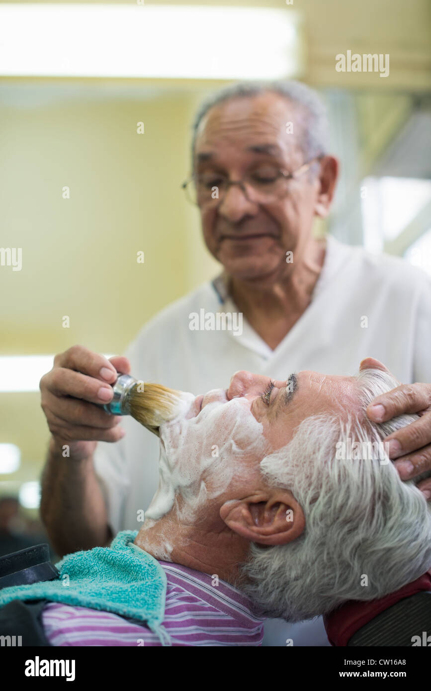 Elderly barber with shave brush applying cream to client in old style