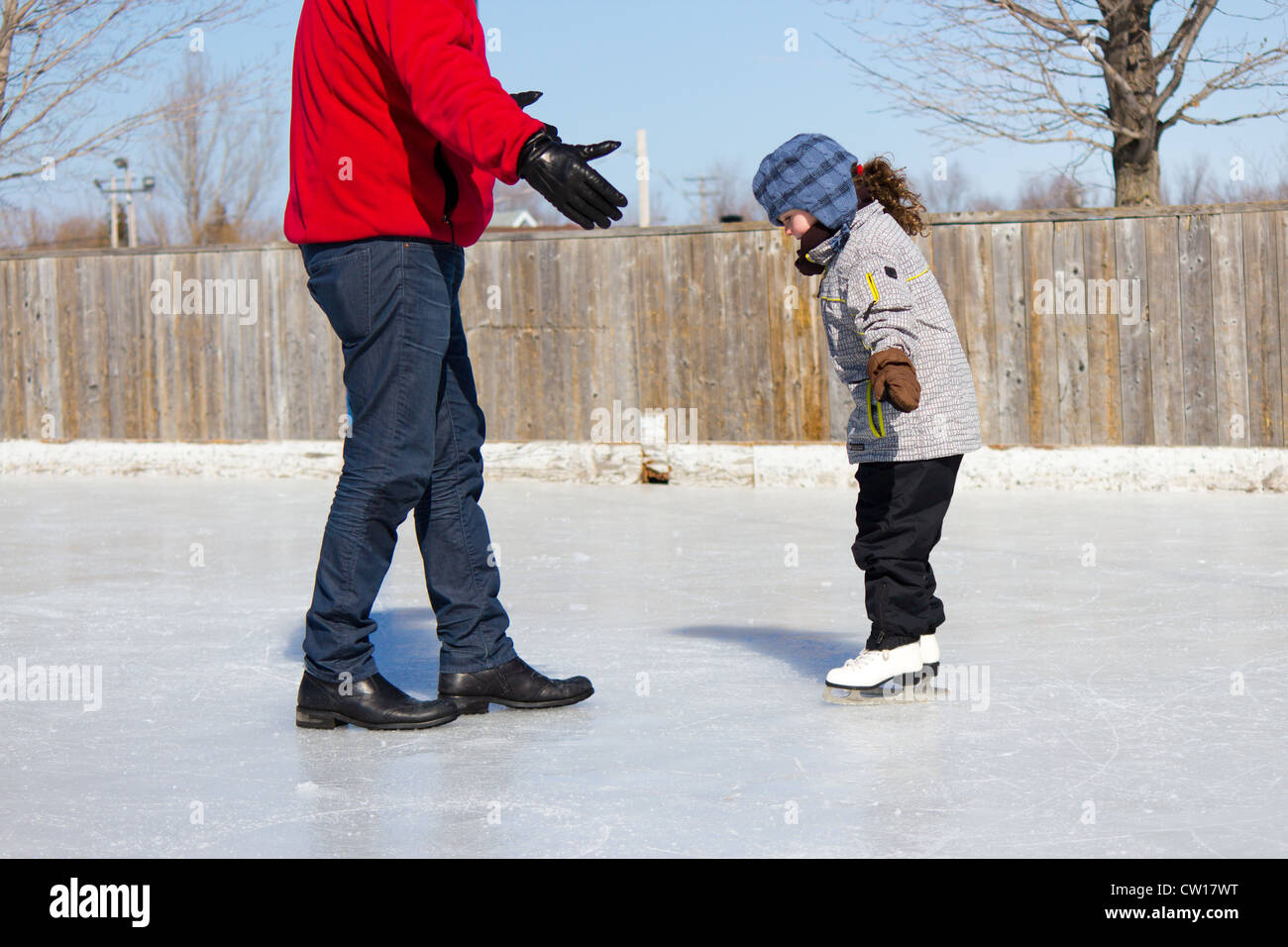 Father teaching daughter how to ice skate at an outdoor skating rink in winter. Stock Photo