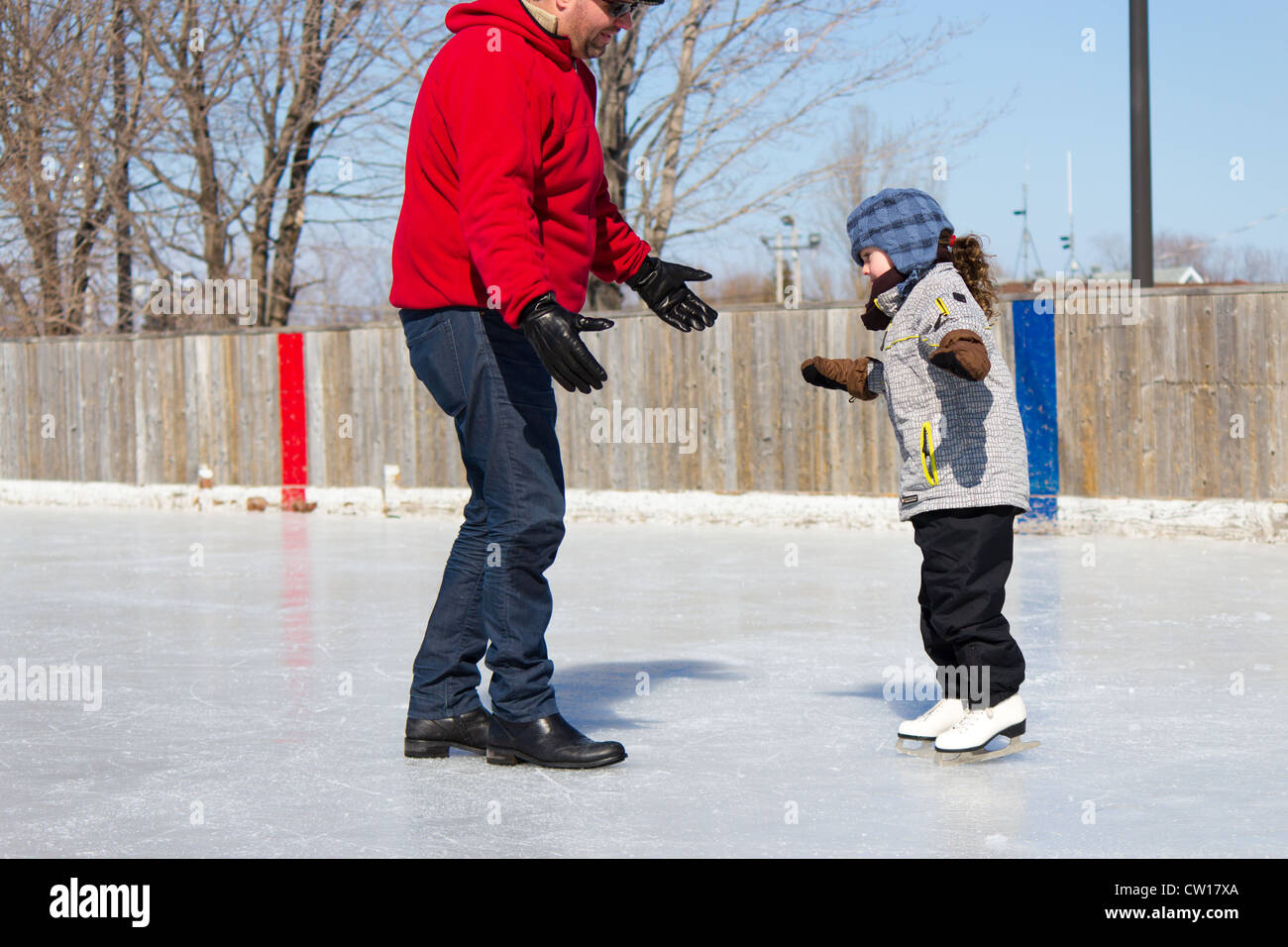 Father teaching daughter how to ice skate at an outdoor skating rink in winter. Stock Photo