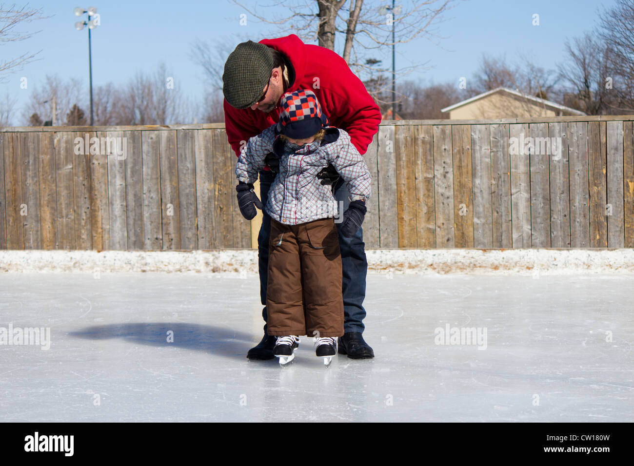 Father teaching son how to ice skate at an outdoor skating rink in winter. Stock Photo