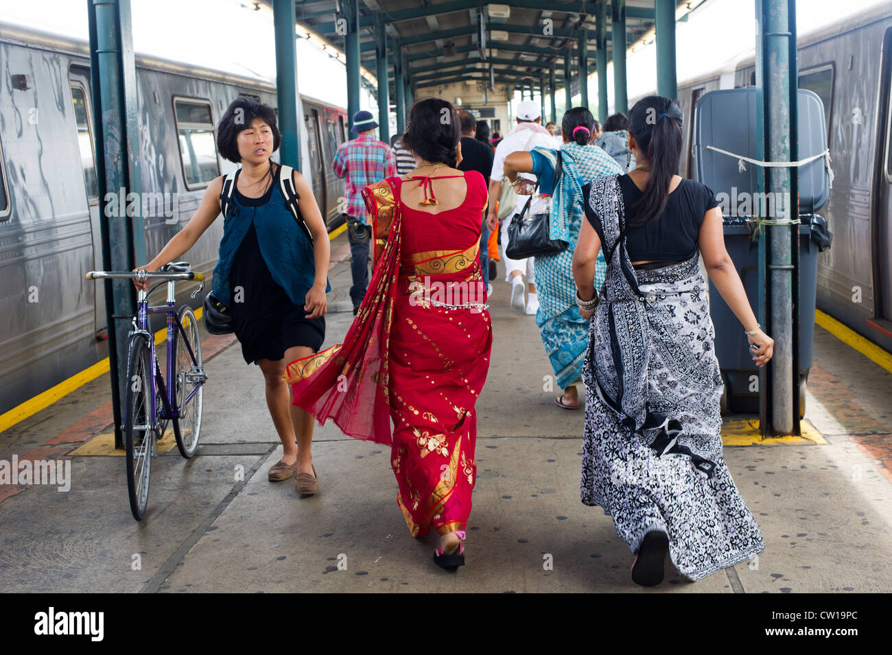 Women dressed in saris pass an Asian woman walking her bicycle at the subway in Richmond Hill in Queens in New York Stock Photo